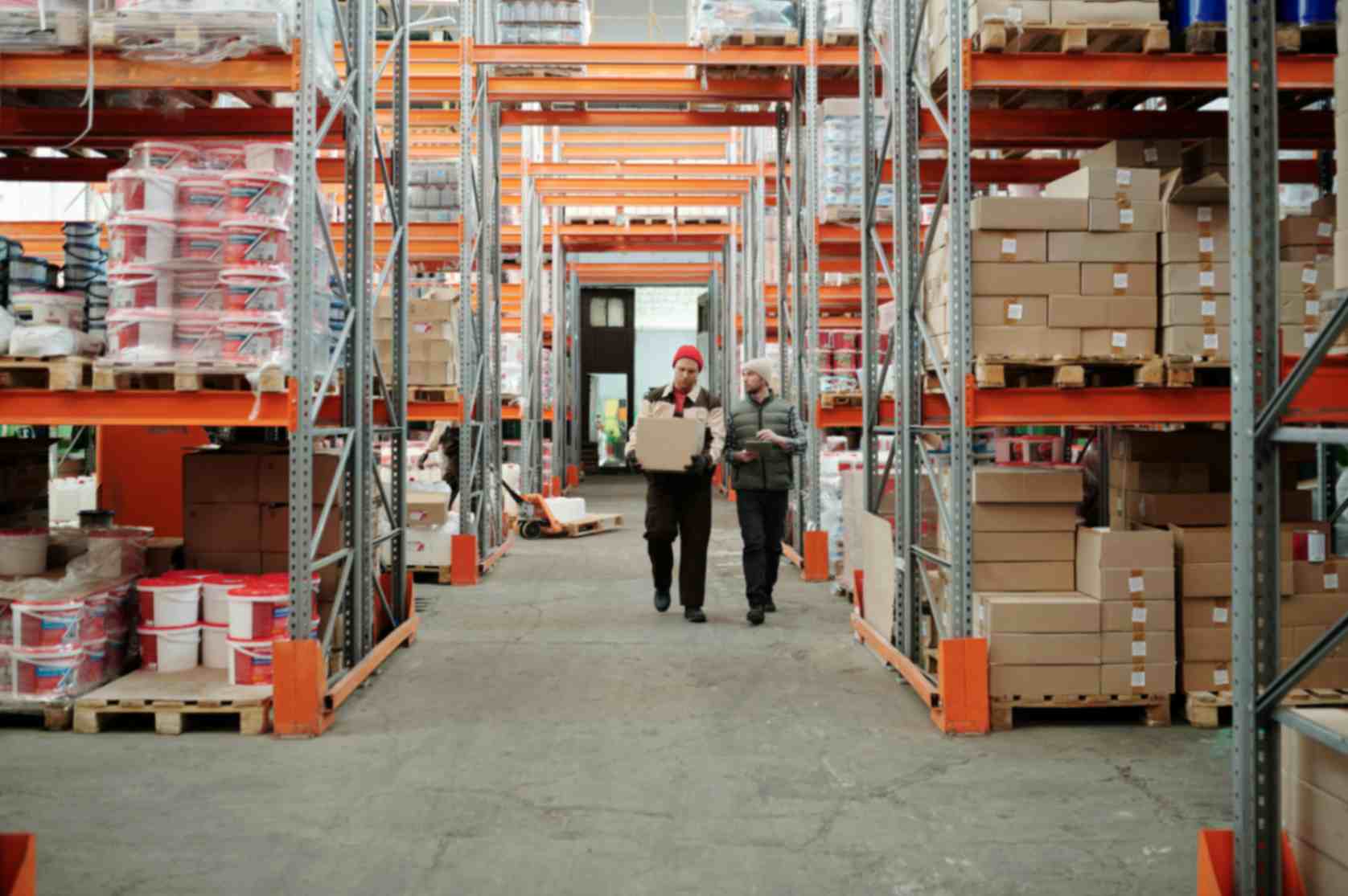 Warehouse workers walking through storage aisles carrying a box