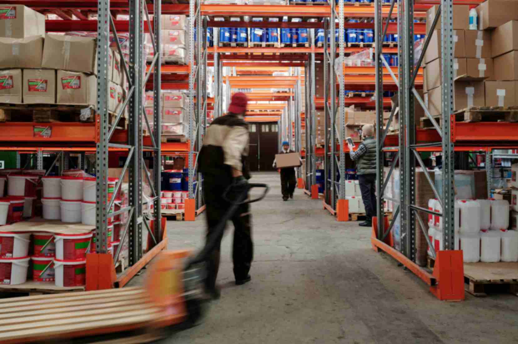 Workers moving goods through warehouse aisles with storage racks and boxed inventory