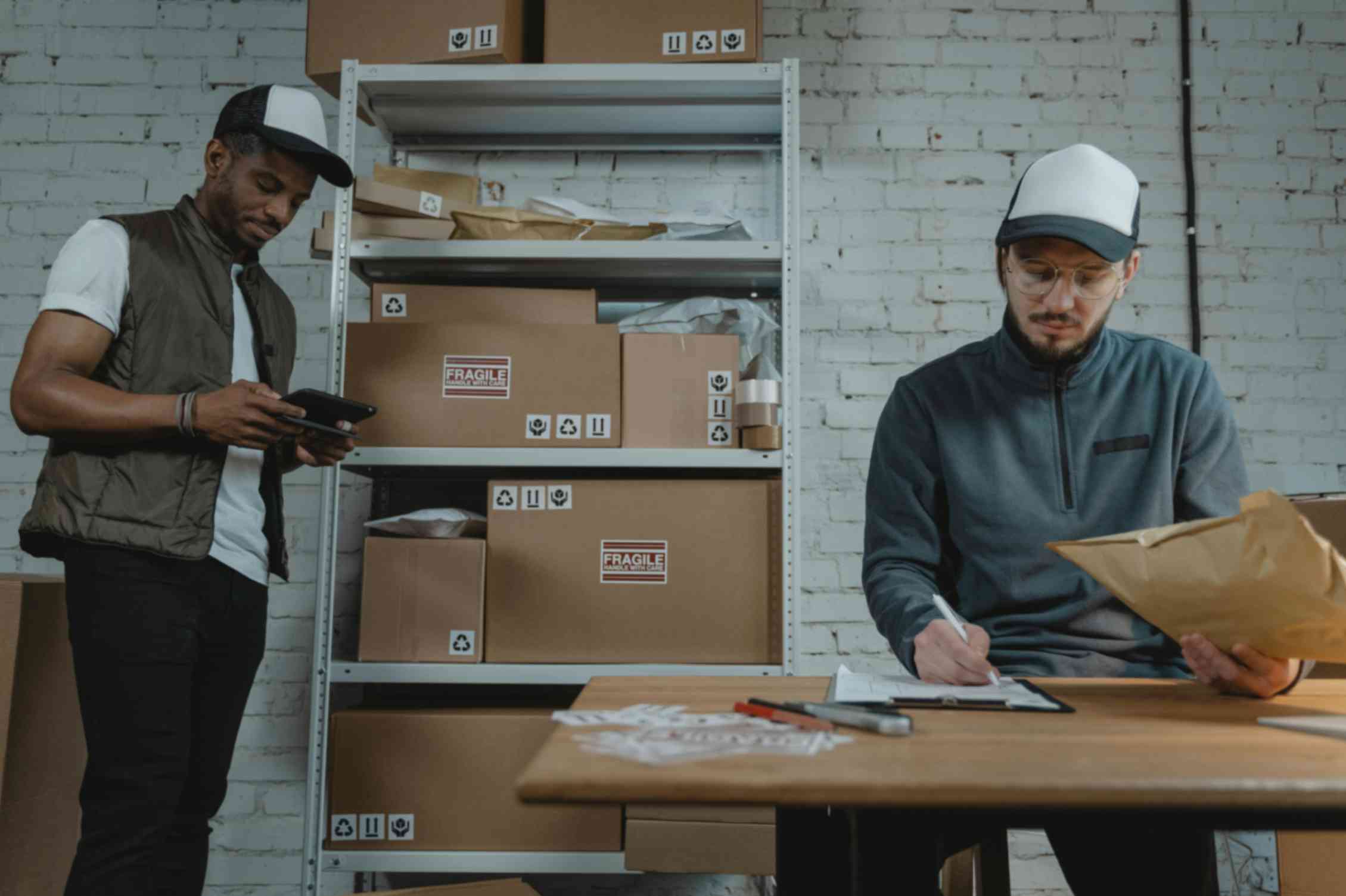 Workers packing and labeling parcels at a table with shelves of boxes behind them