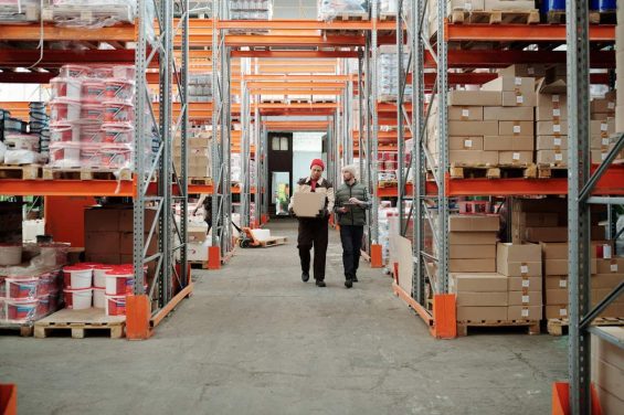 Warehouse workers walk through aisles of stacked inventory.